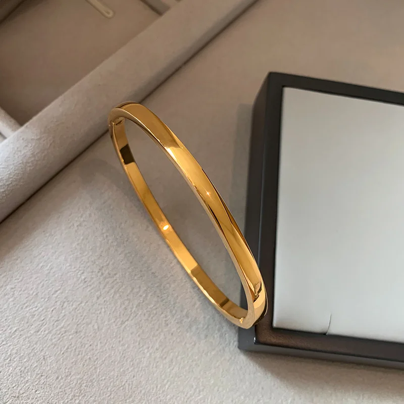 Caffti brand gold-plated bangle with a sleek polished finish, displayed next to a jewelry box on a soft fabric surface
