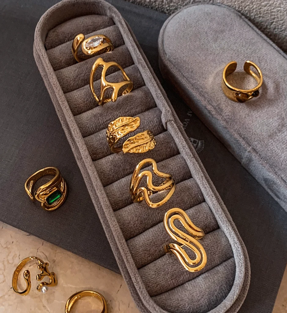Four gold brass open rings with abstract and organic shapes, including one with a small pearl, displayed on fabric.